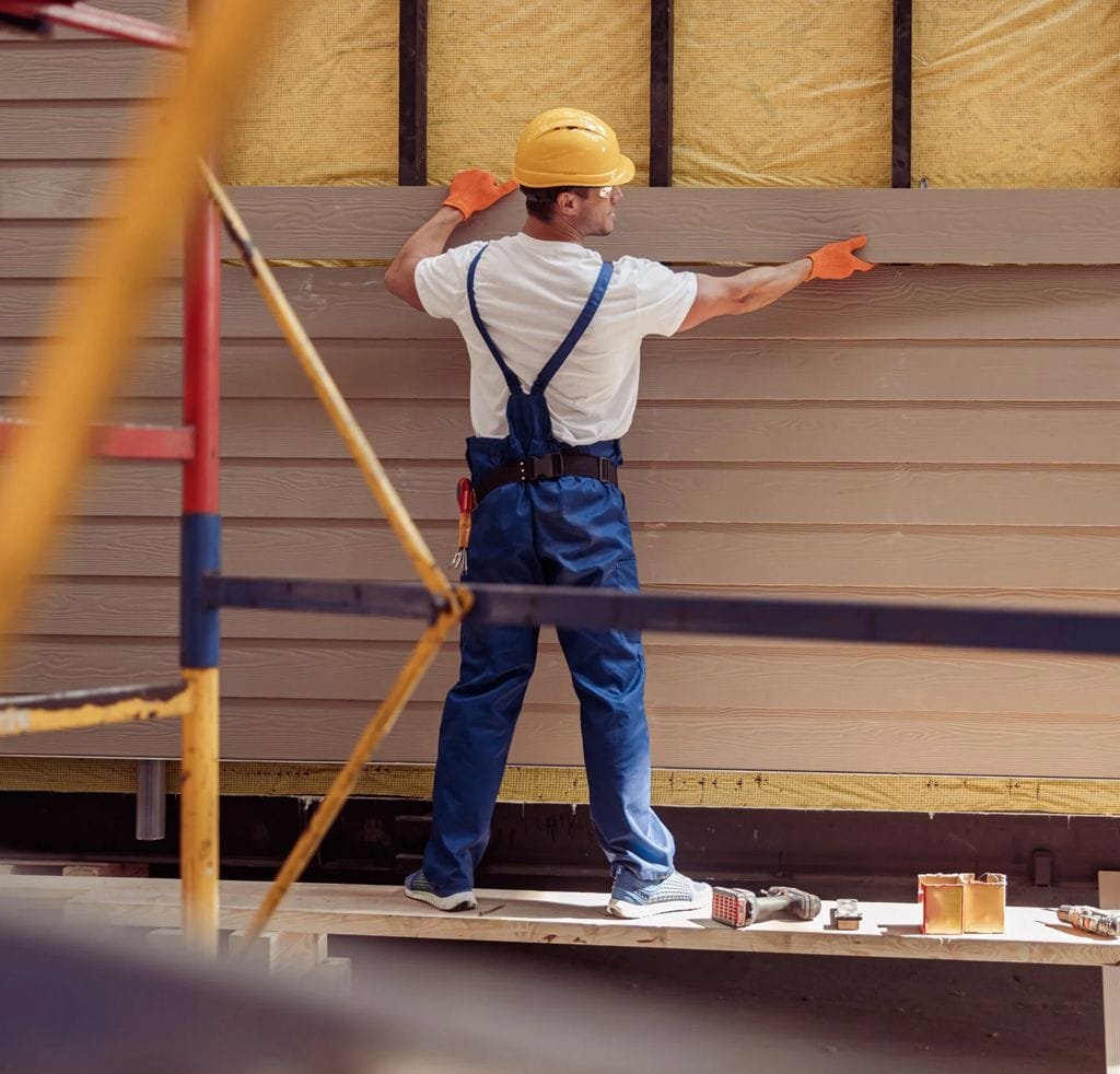 A professional contractor installing new house siding on a residential property exterior