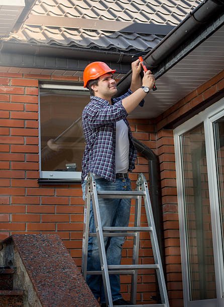 Young worker standing on a step ladder repairing gutters in Granger IN, ensuring proper maintenance to protect the home from water damage.