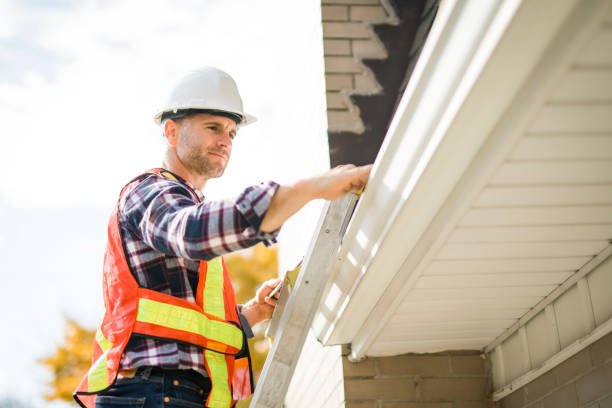 A man with a hard hat standing on steps inspecting the roof for gutter issues in Granger IN, ensuring proper repair to prevent water damage.