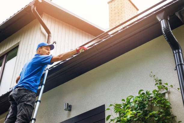 A man on a ladder performing gutter repair in Granger IN, cleaning the roof and ensuring it is well-maintained to prevent water damage.