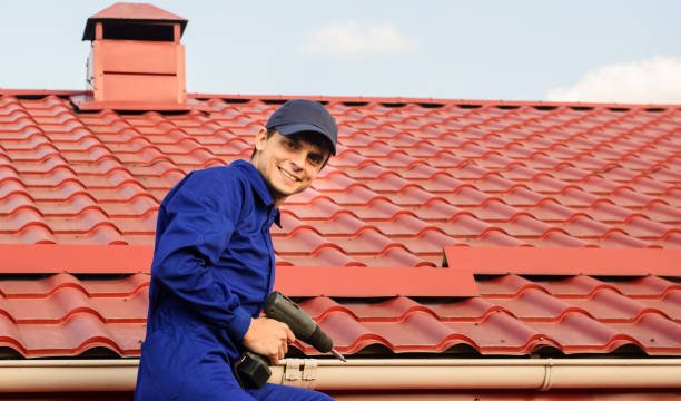Young roofing contractor in blue overalls smiling at the camera while performing affordable roof installation in South Bend IN with an electric screwdriver.