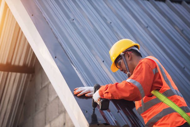 Construction worker performing urgent roof repair on storm-damaged metal sheet using roofing tools and an electric drill for emergency restoration