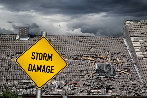 Yellow damage warning sign in front of a roof needing urgent roof repair after severe storm damage from a hurricane or tornado.
