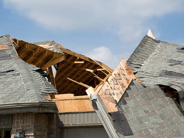 A sign indicating storm damage sits atop a roof, highlighting the urgency for emergency roof repair.
