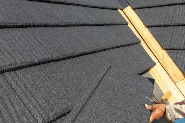 A man installs stone-coated steel roofing on a house, carefully positioning the panels for a secure fit.