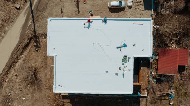 Aerial perspective of a house with several workers engaged in flat roof replacement, surrounded by tools and equipment.
