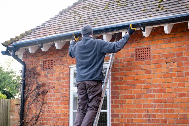 A man with a red hat and gloves works on a pipe for guttering repair in Goshen, IN.
