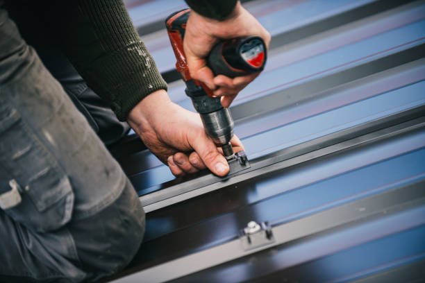 A man operates a drill while installing a metal roof, illustrating the metal roofing installation process.