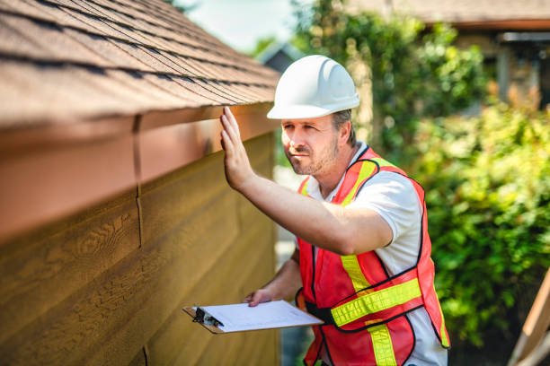 A man in a hard hat and safety vest inspects the gutter of a house, representing Residential Roofing Experts.