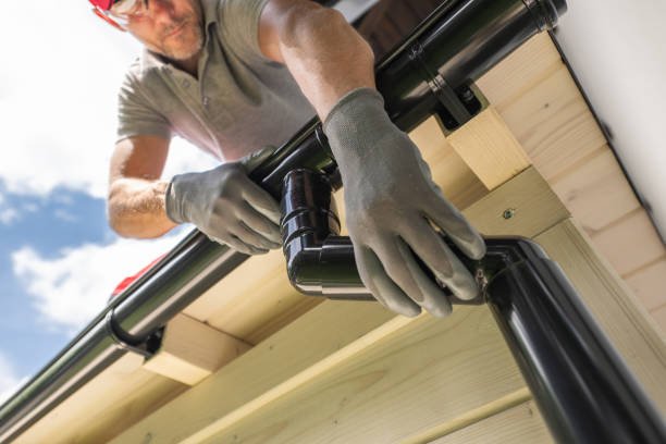A man wearing a red hat and gloves repairs a pipe during guttering work in Goshen , In.