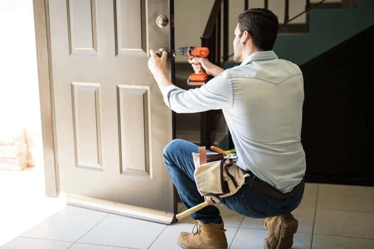 A man using a drill to replace a door, focused on the task at hand in a home improvement setting.